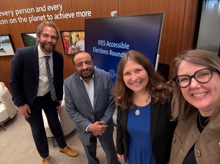 IFES’ Matt Bailey and Virginia Atkinson, Microsoft’s Jenny Lay-Flurrie, and the Special Talent Exchange Programme's Muhammad Atif Sheikh stand for a selfie in front of a sign that reads, 'IFES Accessible Elections Roundtable.'